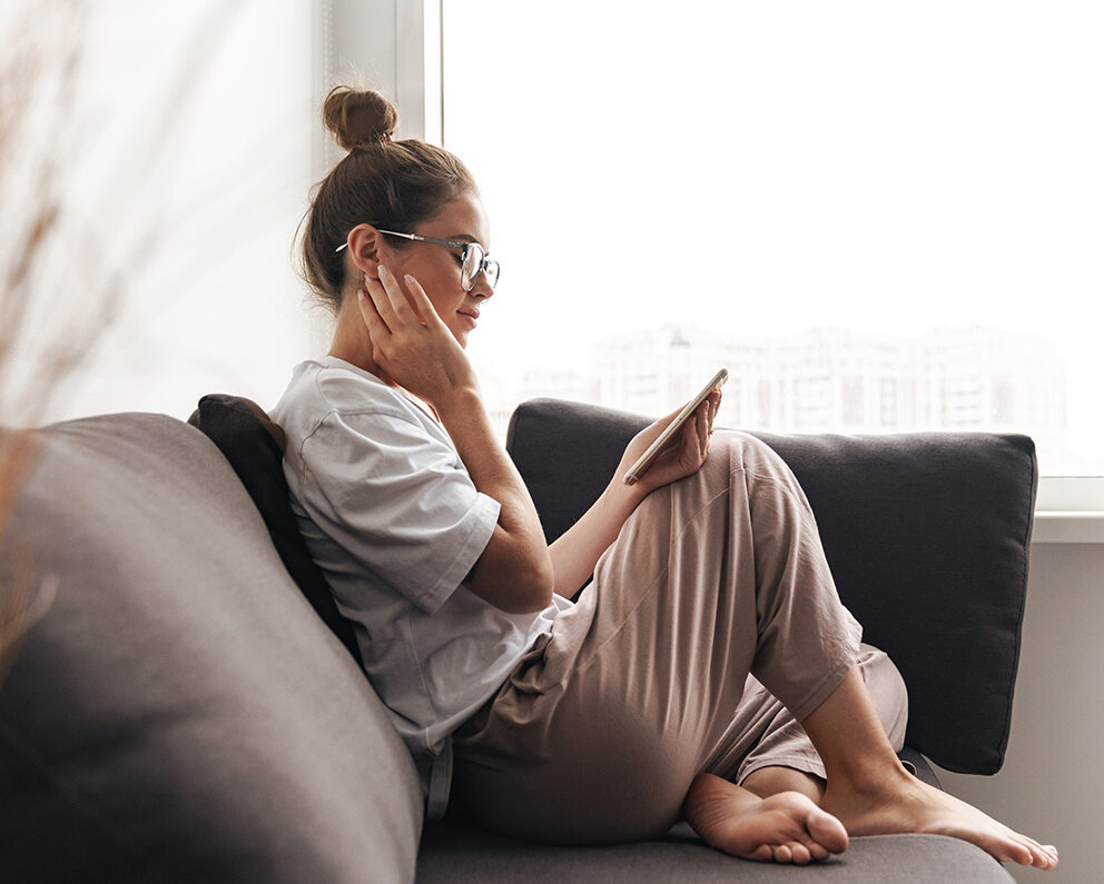 Woman on mobile device on her couch making an appointment with a Fargo Psychiatric Nurse Practitioner